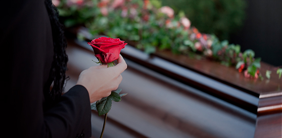 Fotográfia de uma mulher segurando uma rosa em frente a um caixão